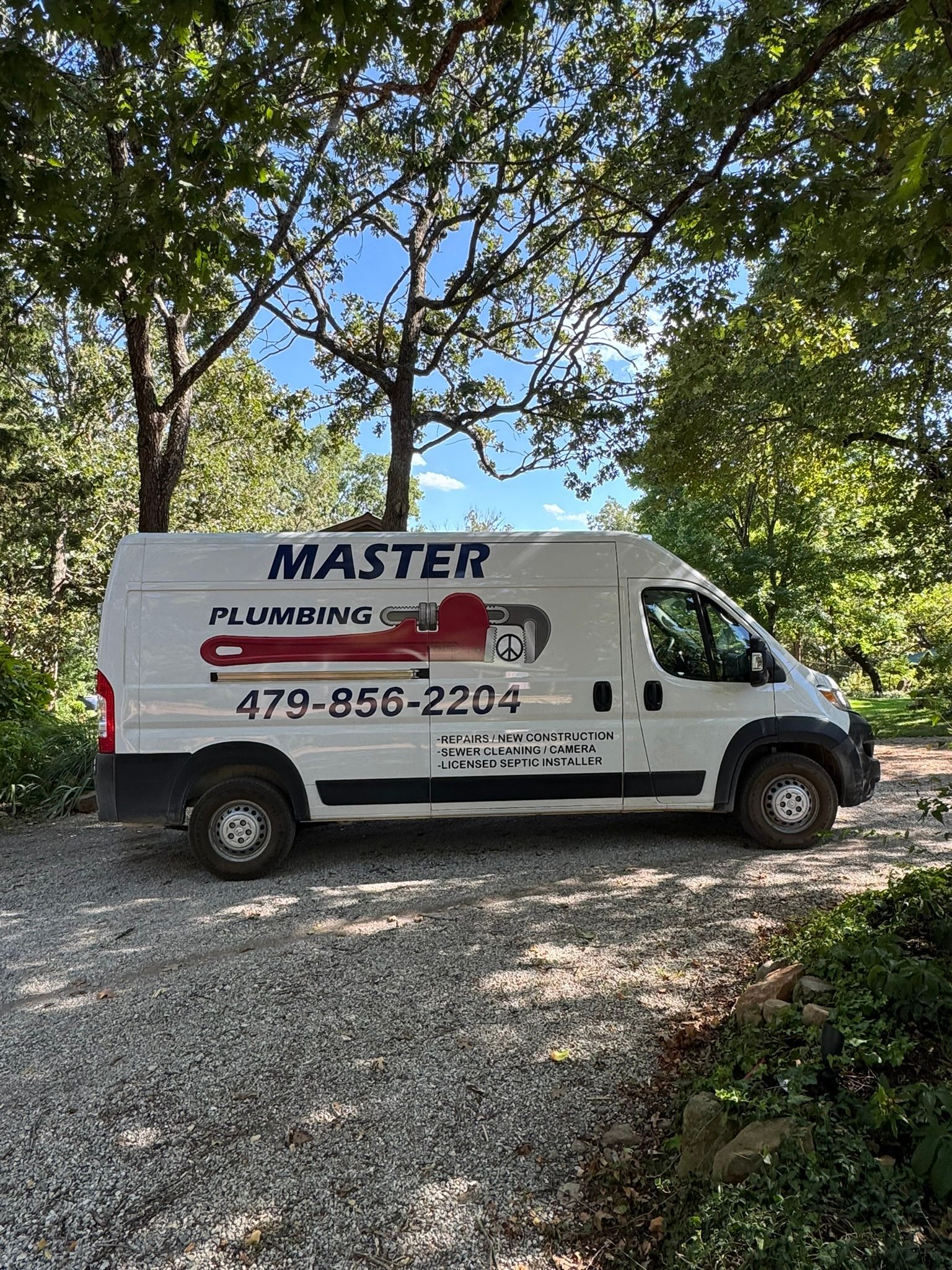 White plumbing service van with “MASTER PLUMBING” and phone number parked on a dirt driveway.