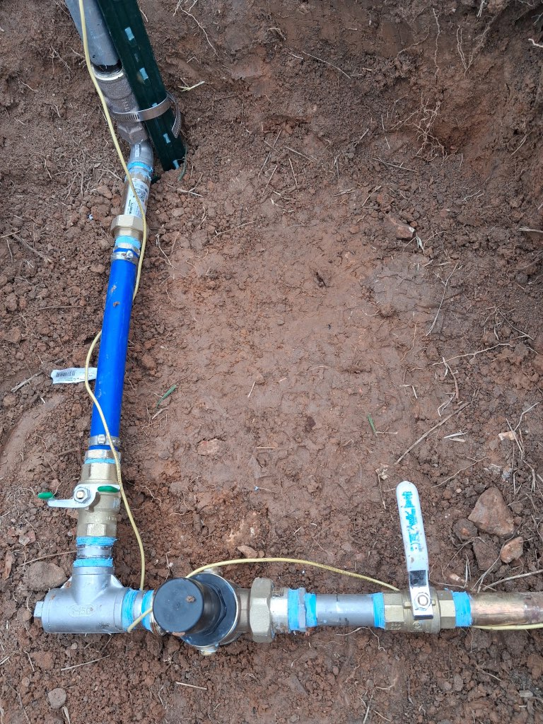 Open utility meter box with pipes, valves, and a yellow water meter against a stucco wall.