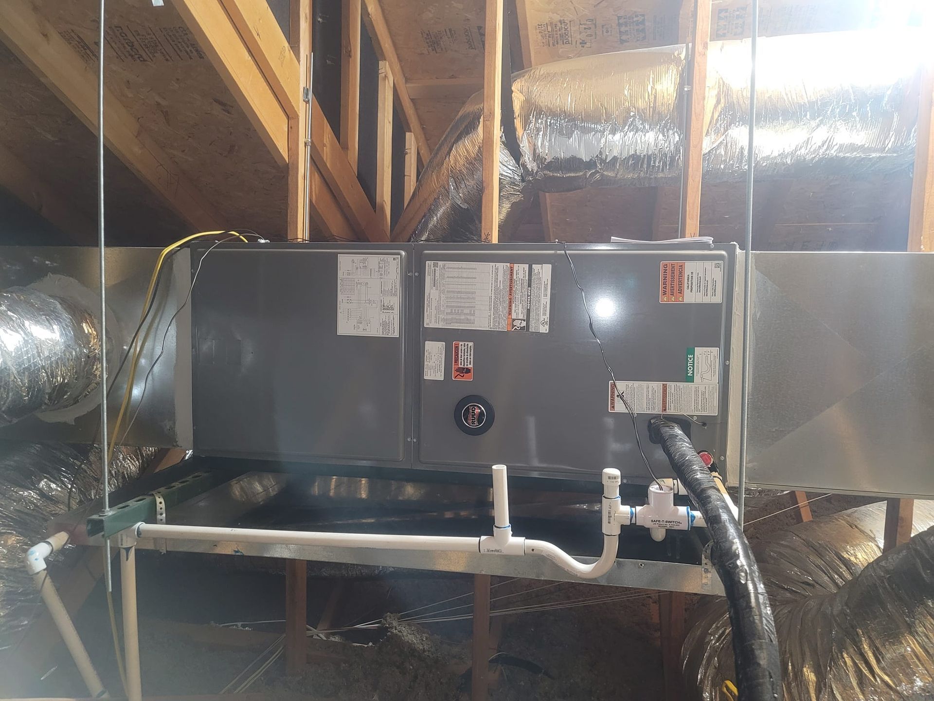 HVAC unit in an attic with ductwork, PVC pipes, and wooden beams.