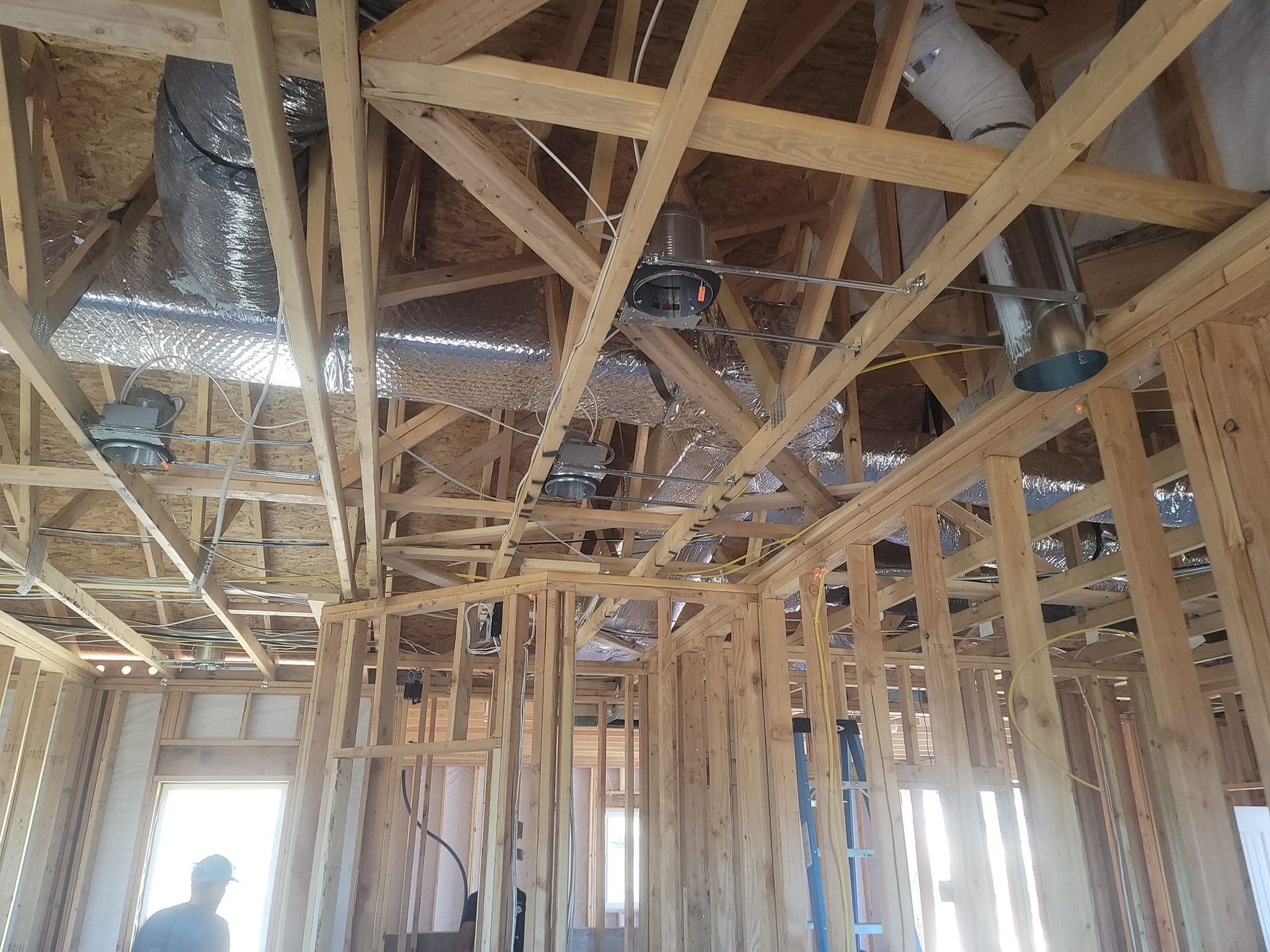 Interior view of a building frame with wooden beams, ducts, and insulation visible. A person is standing.