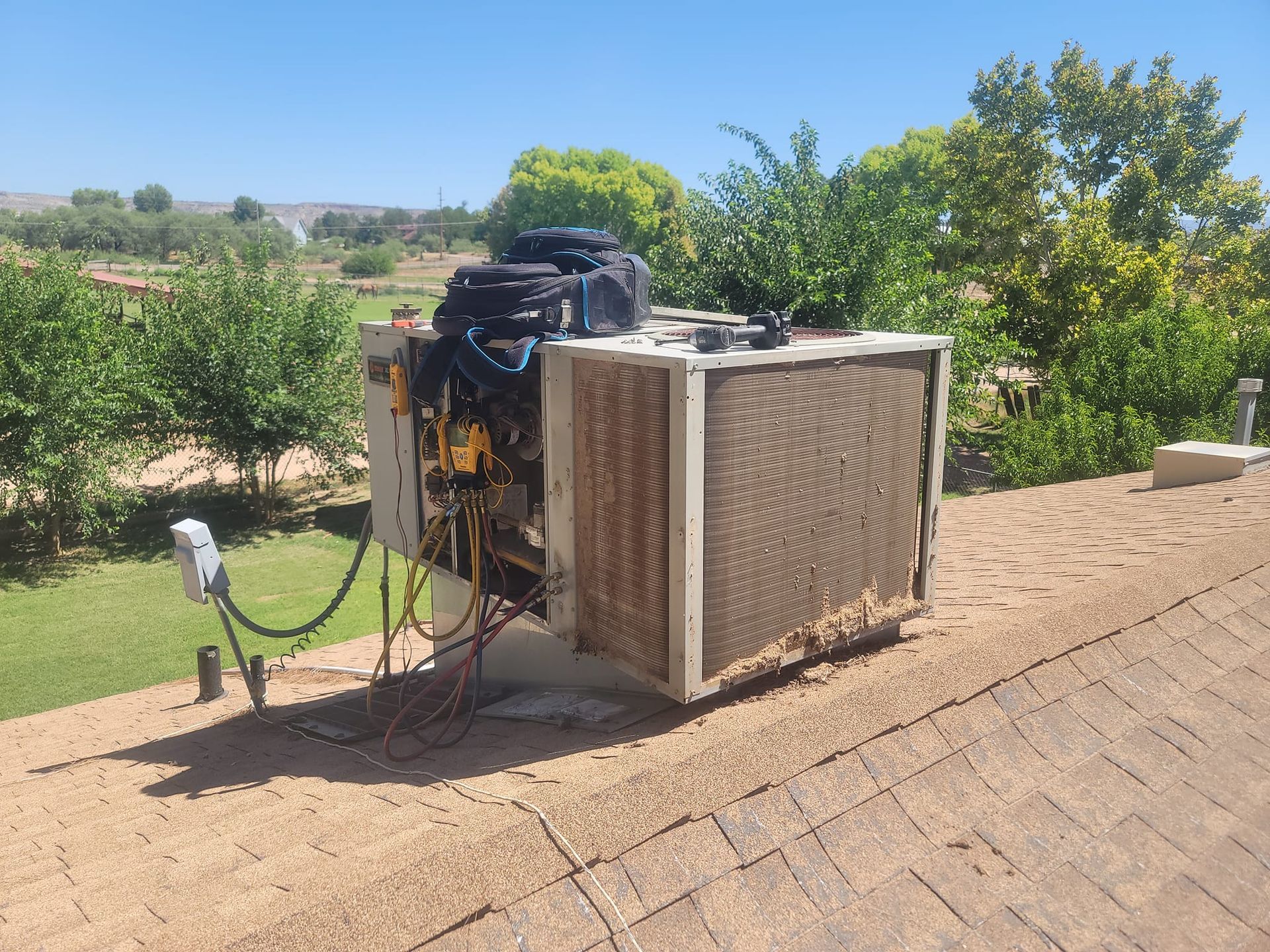 HVAC unit on a rooftop. A black toolbox sits on top. Trees and a green lawn are in the background.