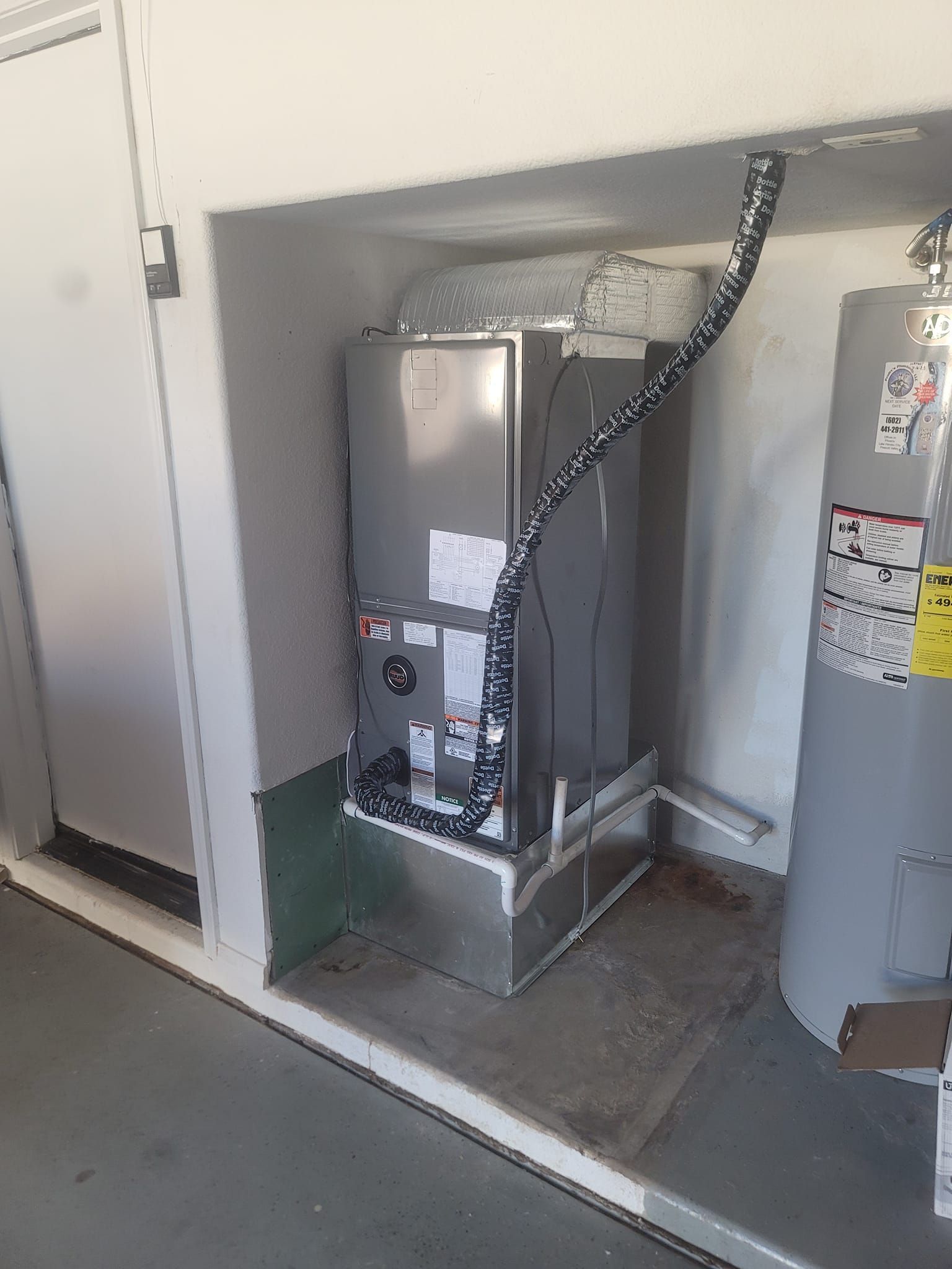 HVAC unit and water heater in a utility closet. Ductwork and insulated refrigerant line visible.