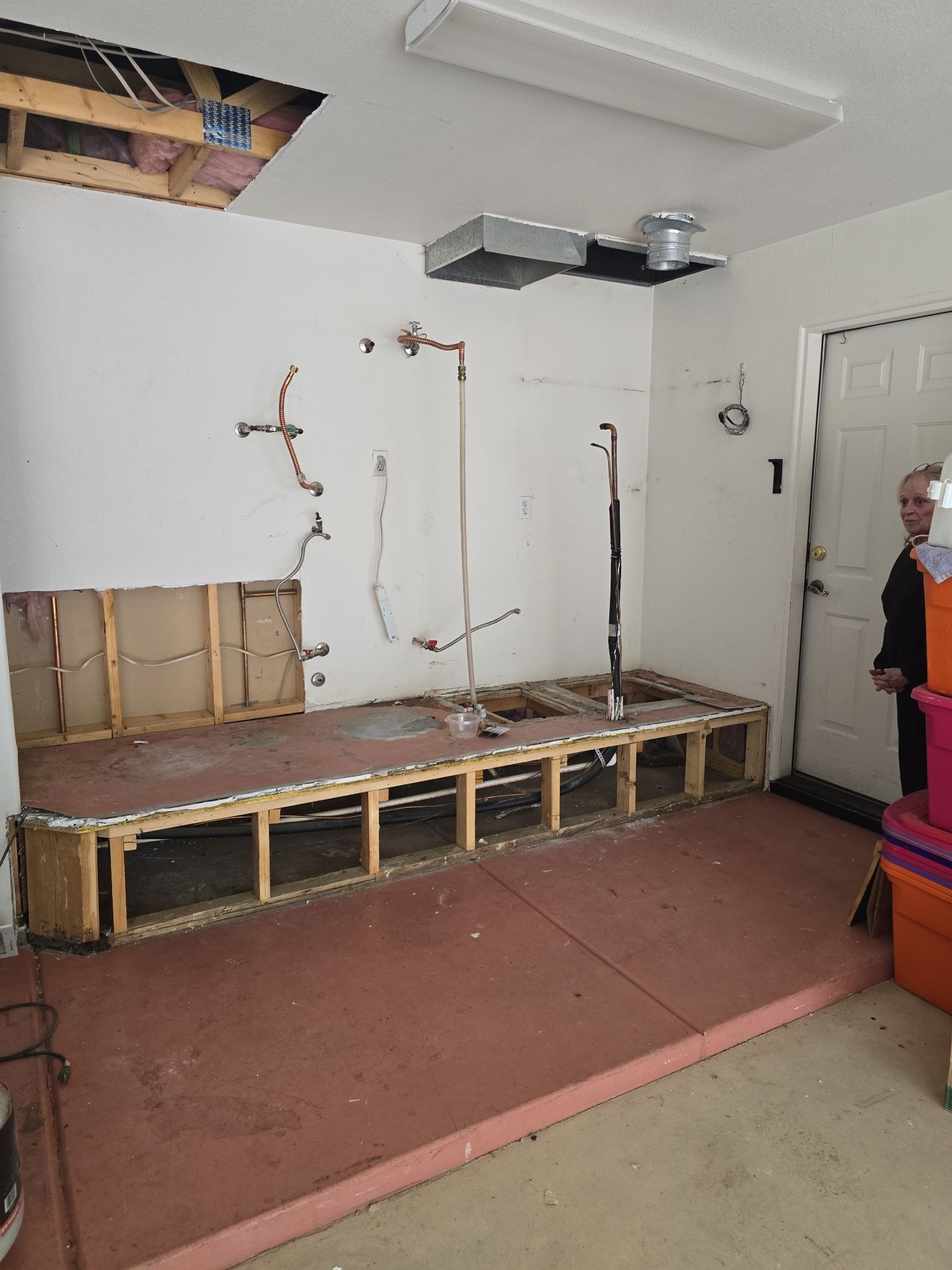 Garage interior with exposed framing, pipes, and a person standing near a door.