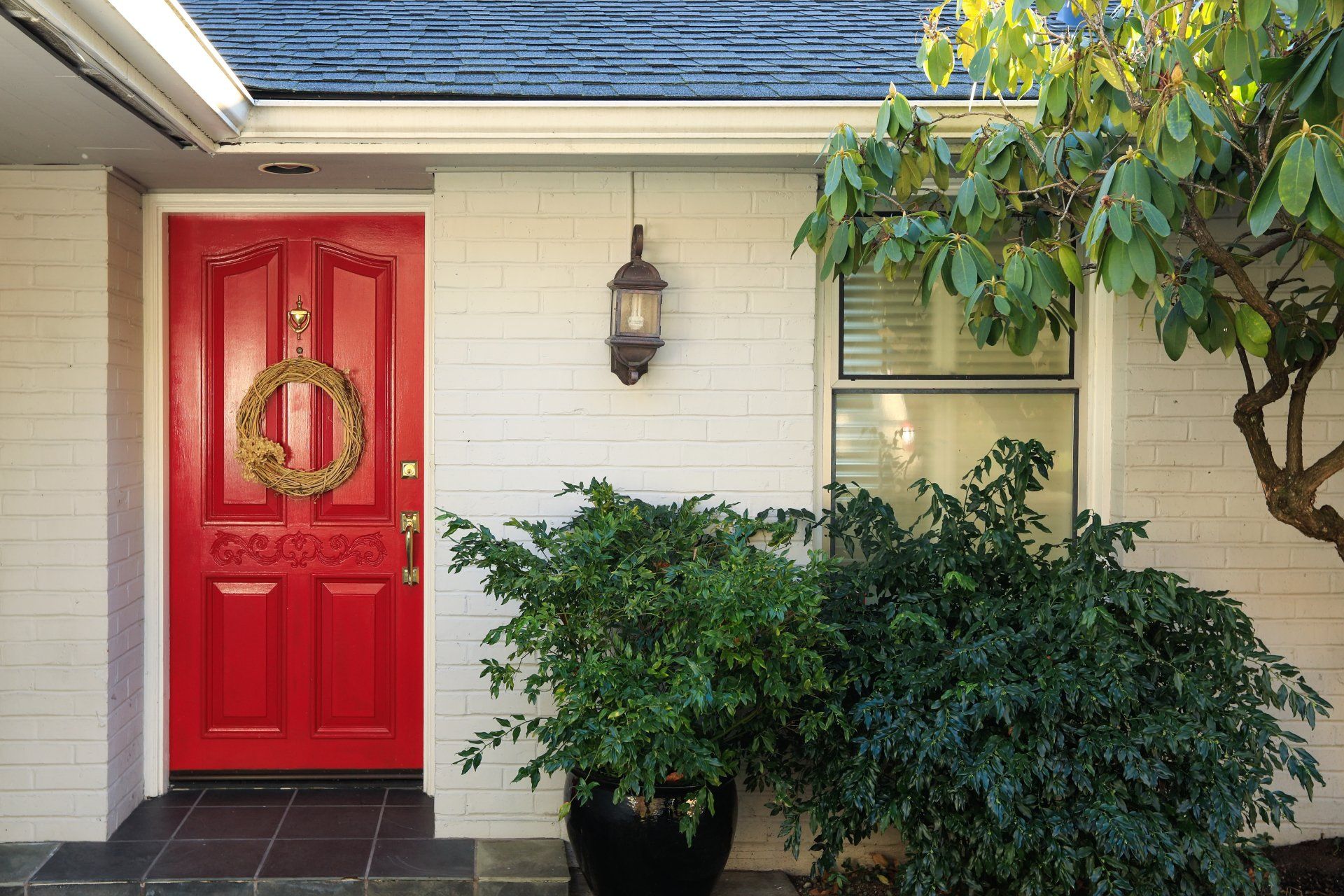 a red door with a wreath on it is on a white brick house