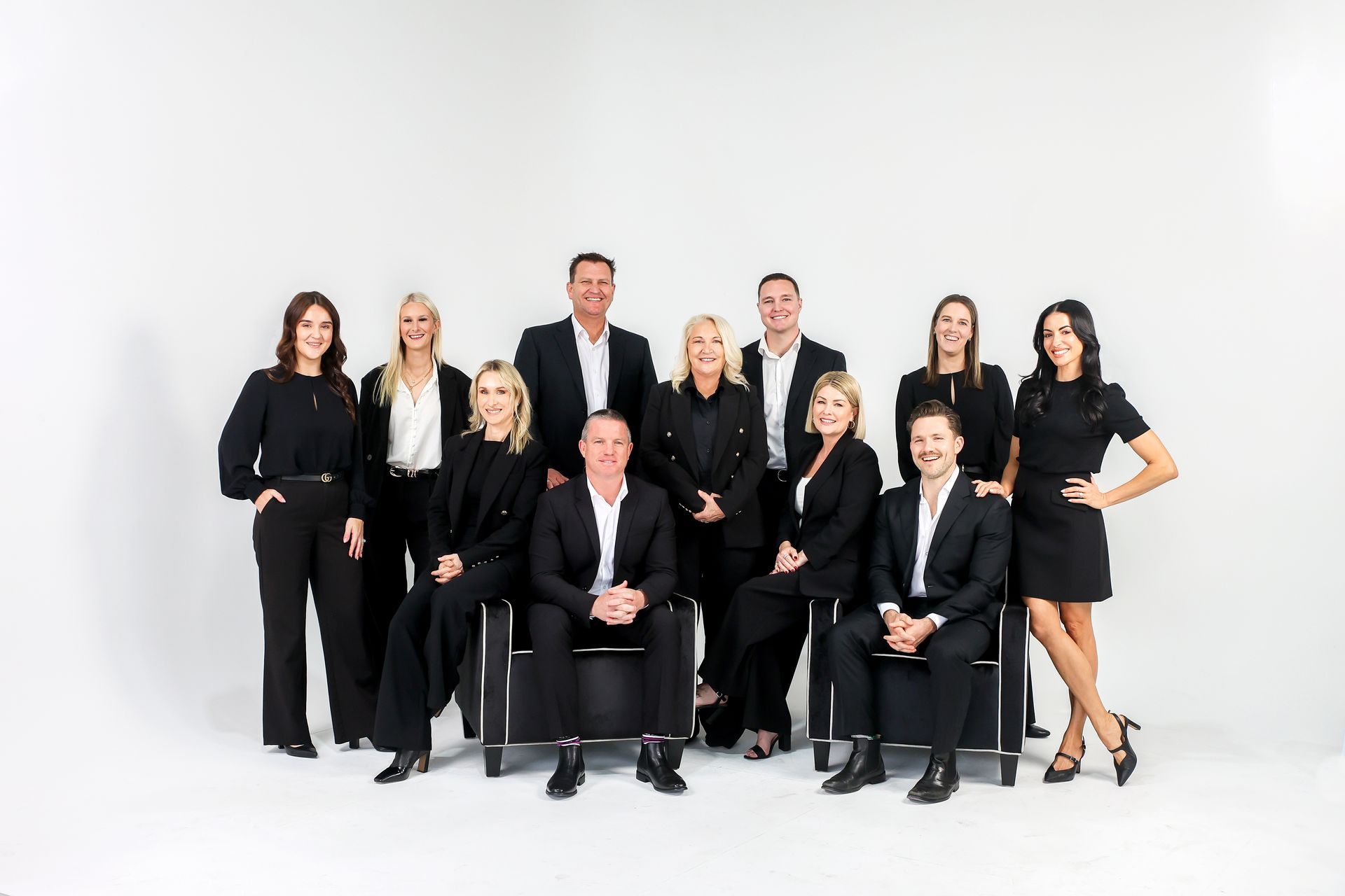 Group of people in black suits posing in front of a white background.