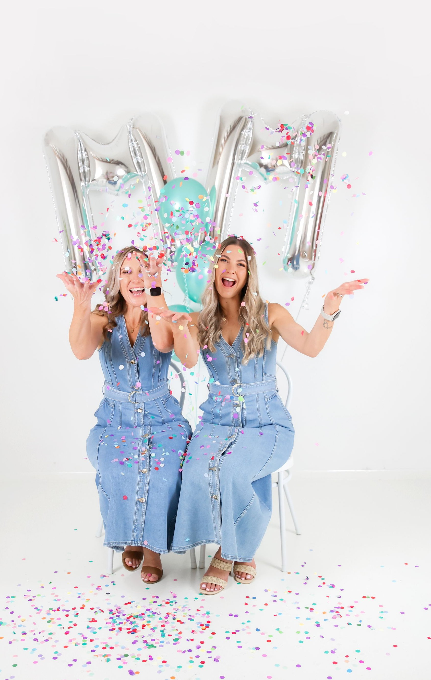 Two women throwing confetti, sitting with balloons that spell