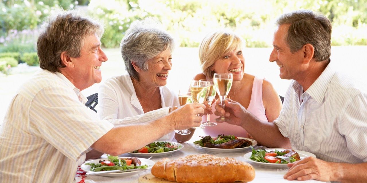 Four people toasting glasses of wine at an outdoor table with food.