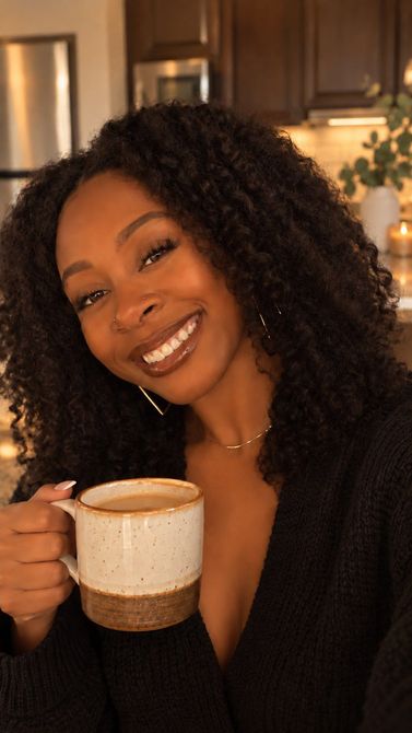 Denae Williams smiling in a warm kitchen while holding an MFTea With Me mug