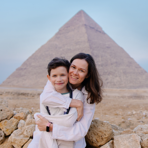 A woman is holding a child in front of a pyramid.