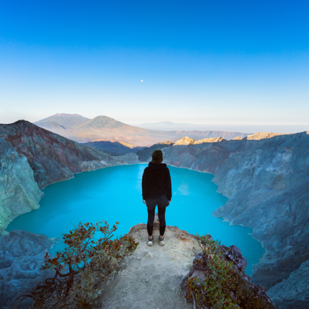 A person is standing on top of a mountain overlooking a lake.