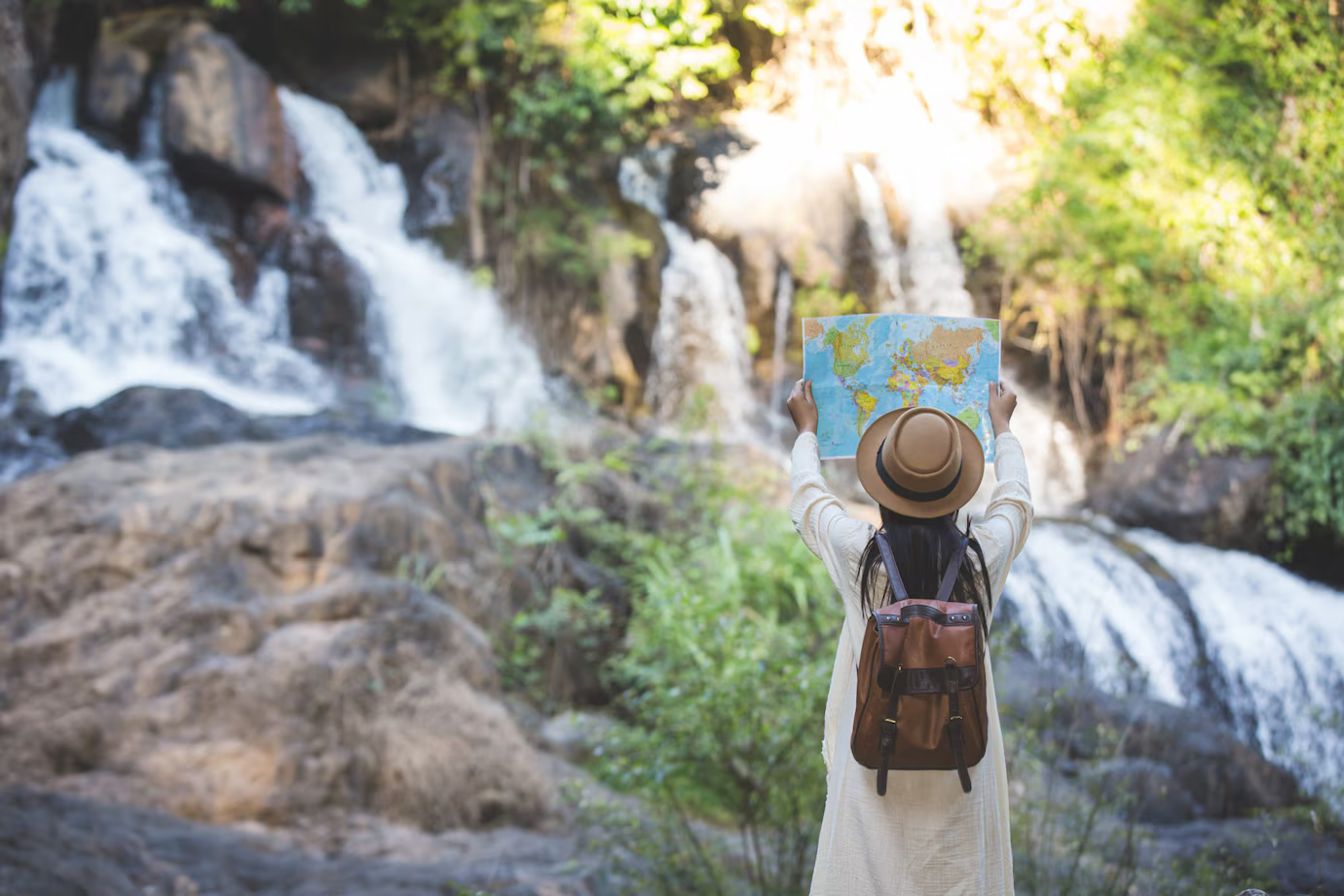 A woman is holding a map in front of a waterfall.