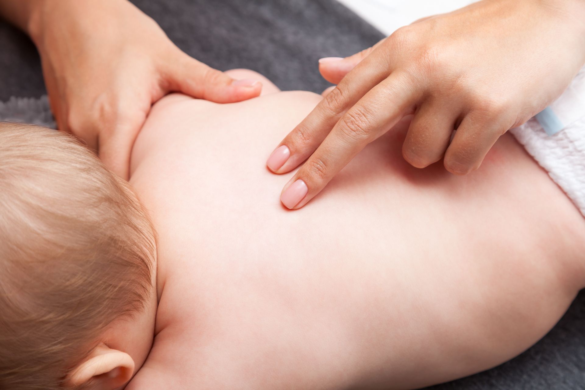 Hands gently massage a child’s bare back on a towel.