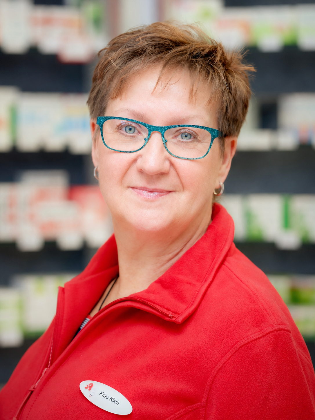Frau mit Brille, rotem Oberteil, lächelnd, in einem Geschäft.