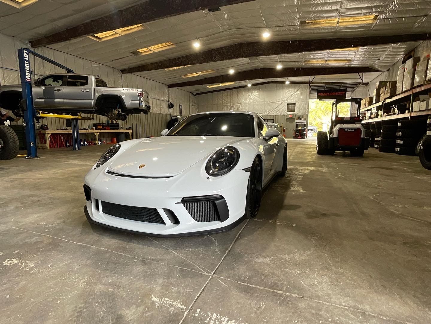 White Porsche sports car inside a garage; truck on lift in background | Marshside Motors