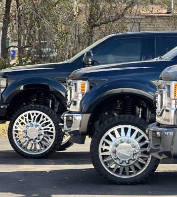 Three dark-colored Ford trucks with large chrome wheels parked outside | Marshside Motors