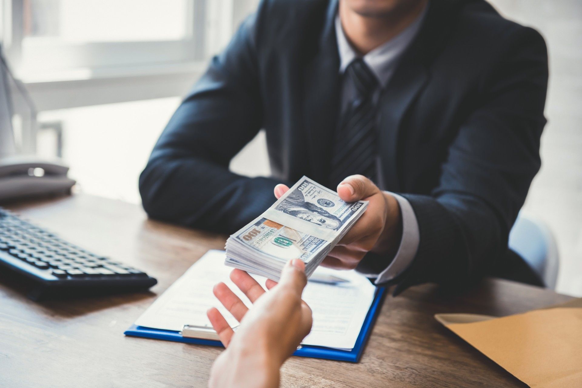 A man in a suit is giving a woman a stack of money.