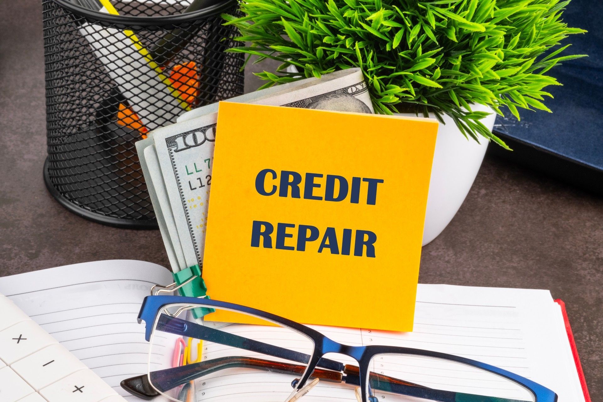 A yellow sticky note that says credit repair is sitting on top of a notebook.