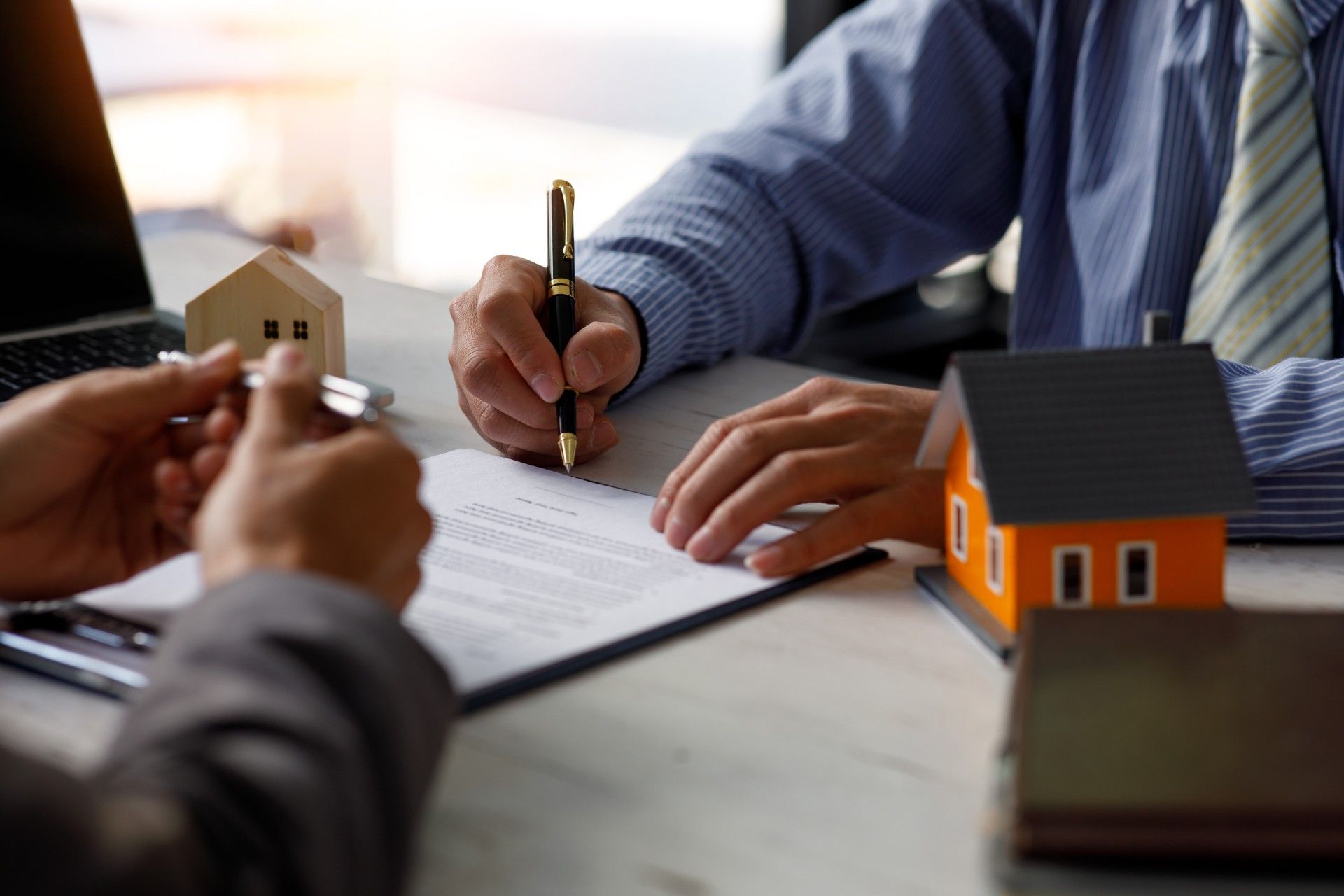 A man is signing a document next to a model house.