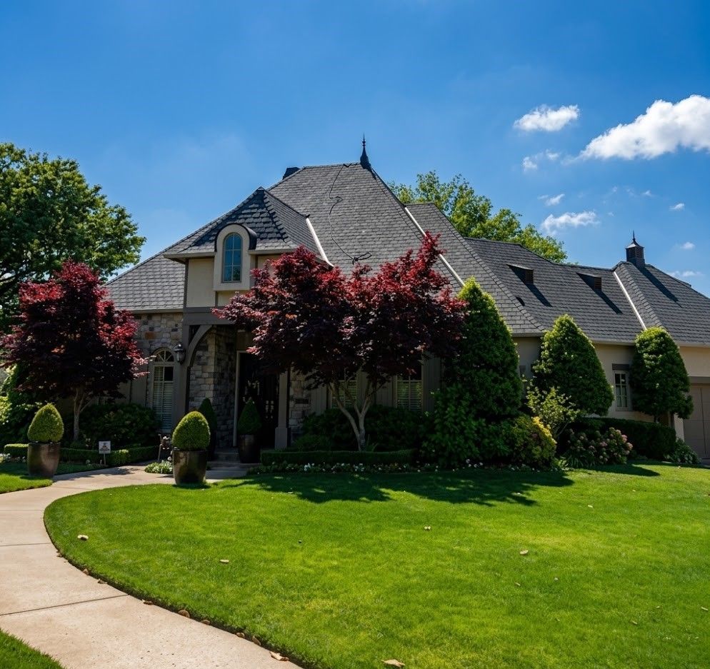Large suburban house with stone facade, curved walkway, and lush green lawn under a blue sky