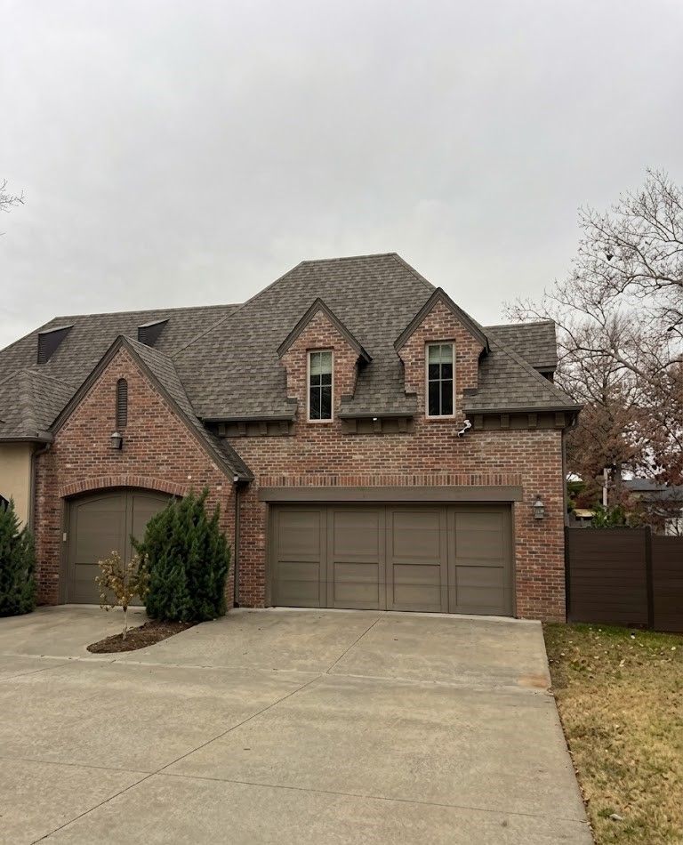 Brick suburban house with two garages and a concrete driveway under an overcast sky
