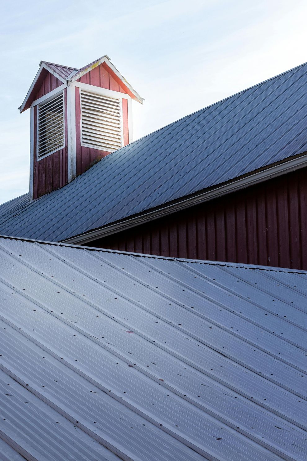 Red barn roof with white trim and a small cupola under a clear blue sky