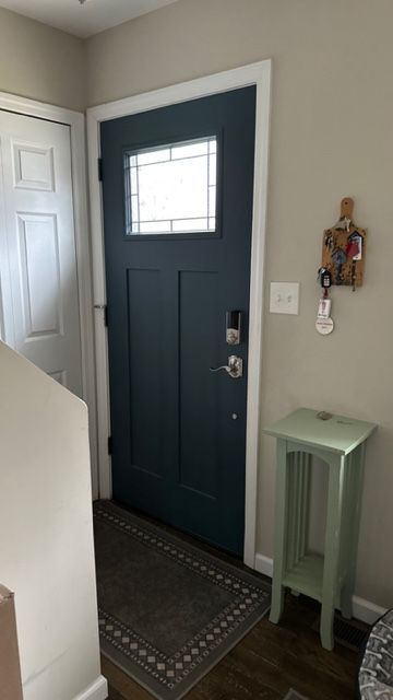 A dark blue front door with a window, white trim, a key rack, and a small green pedestal table in an entryway.