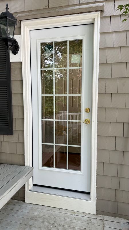 White 15-lite glass door with gold handles, set in a light grey shingled wall next to an outdoor lantern and deck.