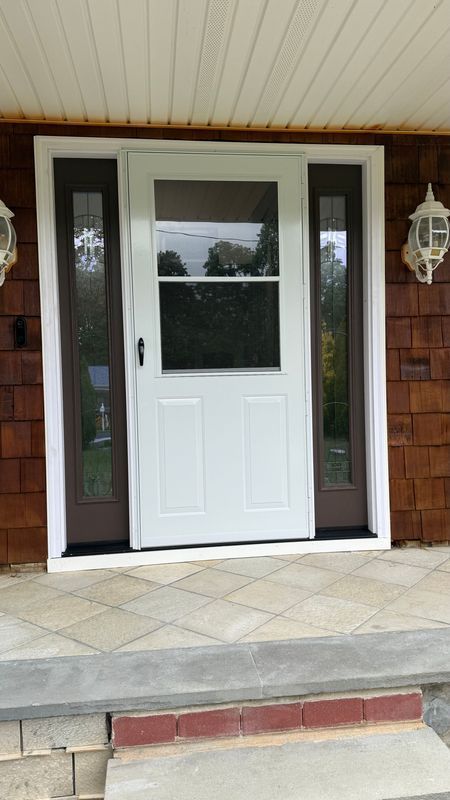 A white storm door with a window at the top, flanked by two sidelights, mounted on a house with brown shingle siding.