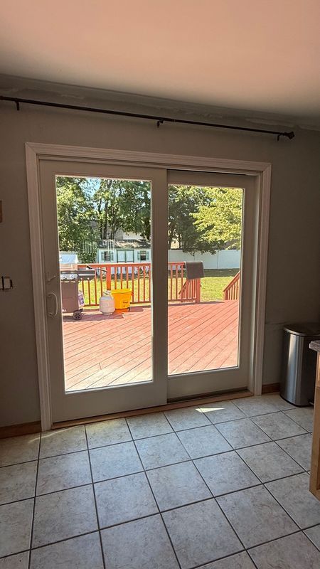 A sliding glass door viewed from inside a room with tiled floors, opening onto a wooden deck in a backyard.