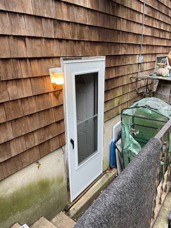 A white storm door installed on the exterior of a home with cedar shake siding, illuminated by an outdoor wall lamp.