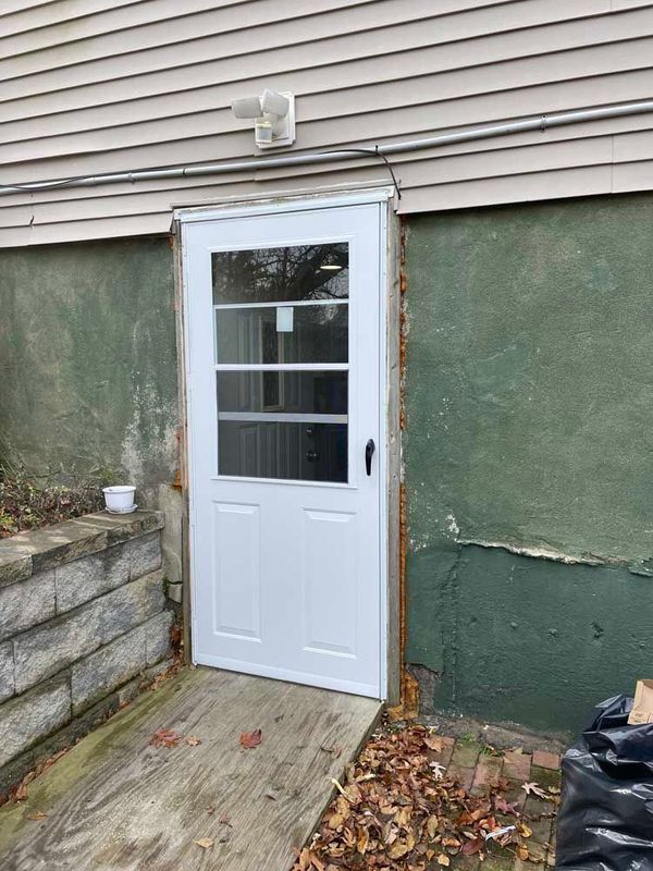A white half-glass door installed in a rough green concrete foundation wall next to a wooden ramp.