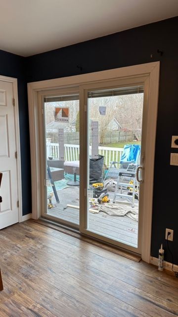 A sliding glass door with a white frame set into a navy blue wall, looking out onto a deck with construction tools.