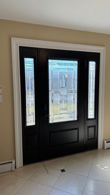 Black front door with decorative frosted glass panels, surrounded by white molding and light tan walls in a tiled foyer.
