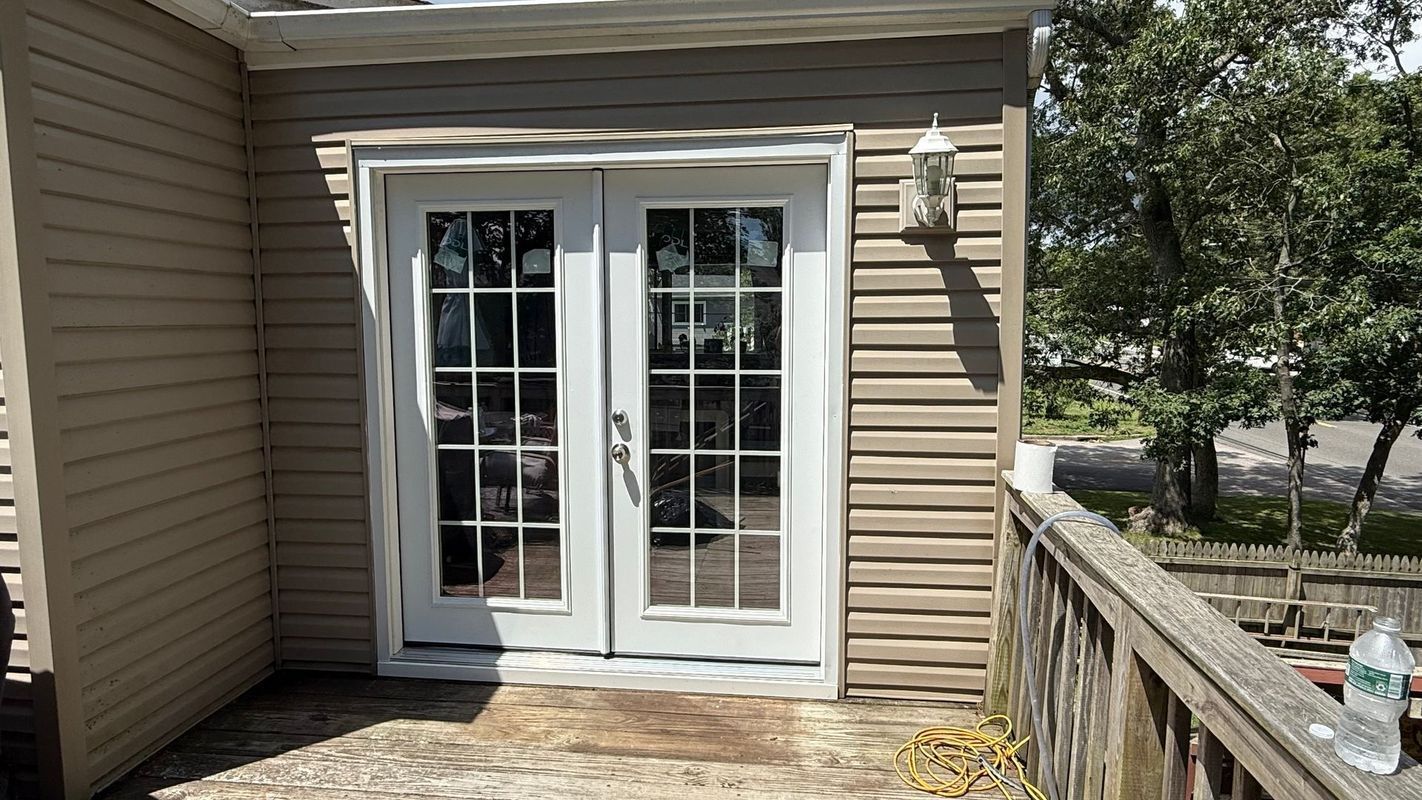 White French doors with a grid pattern on a tan-sided exterior wall next to a wooden deck railing.