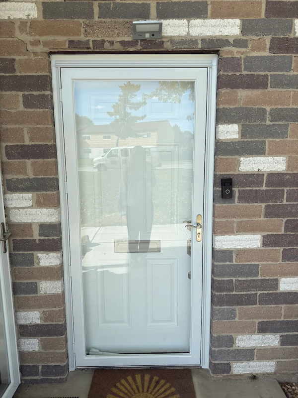 A white storm door with a large glass panel and white bottom section, set in a multicolored brick exterior wall.