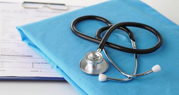 Uno stetoscopio su una cartella blu accanto a un blocco appunti, a suggerire un contesto medico o sanitario.