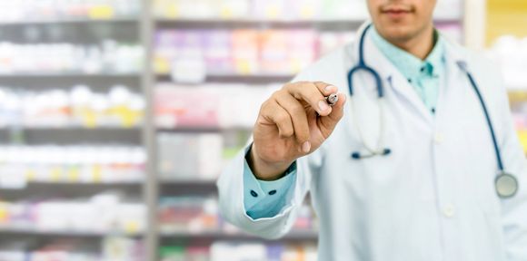 Un medico in camice bianco e stetoscopio tiene in mano una pillola in un corridoio di una farmacia.