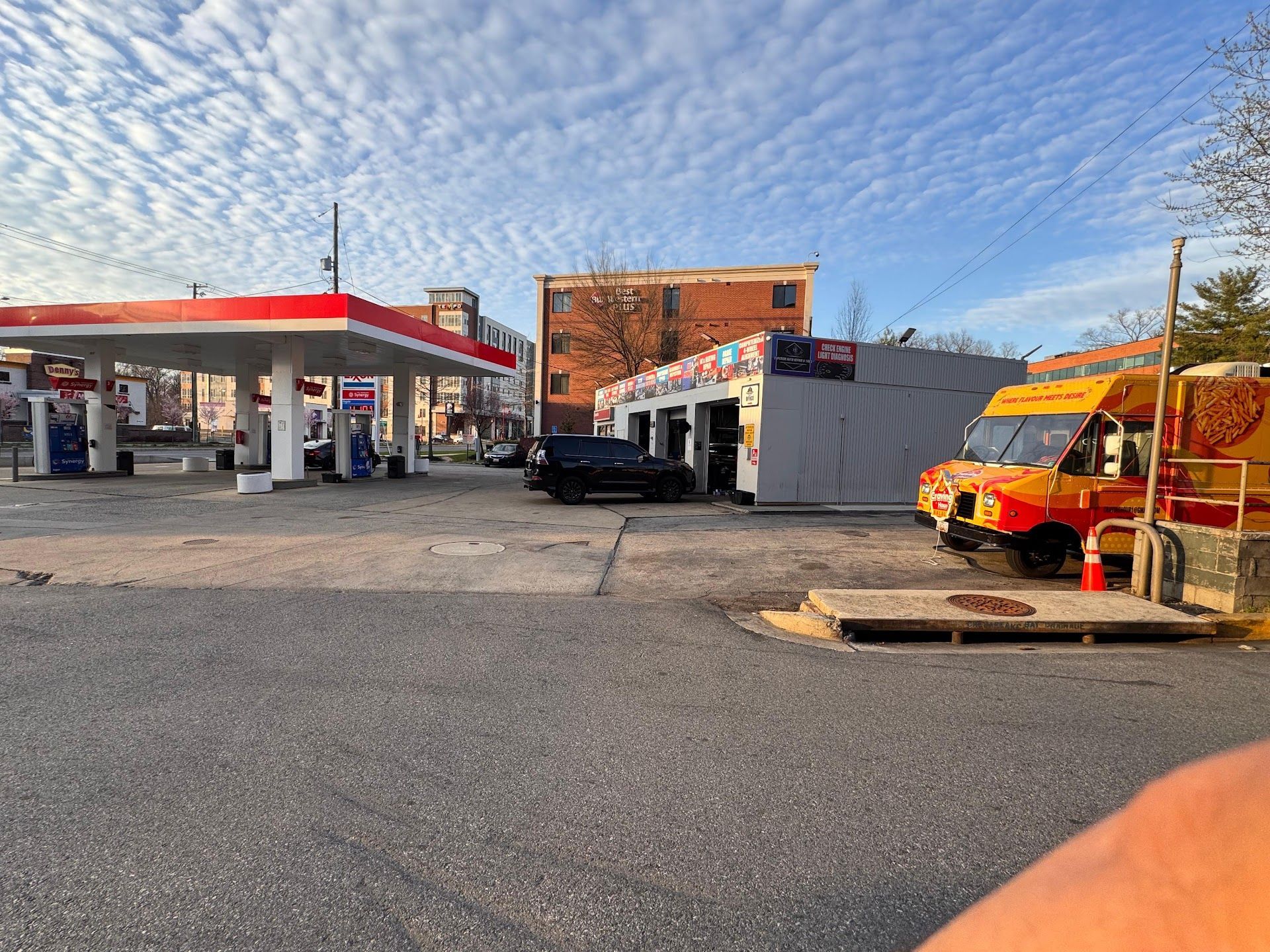 An outdoor scene featuring a gas station with a red-and-white roof, a car service bay, and a bright yellow food truck. | Superior Auto Repair and Tires