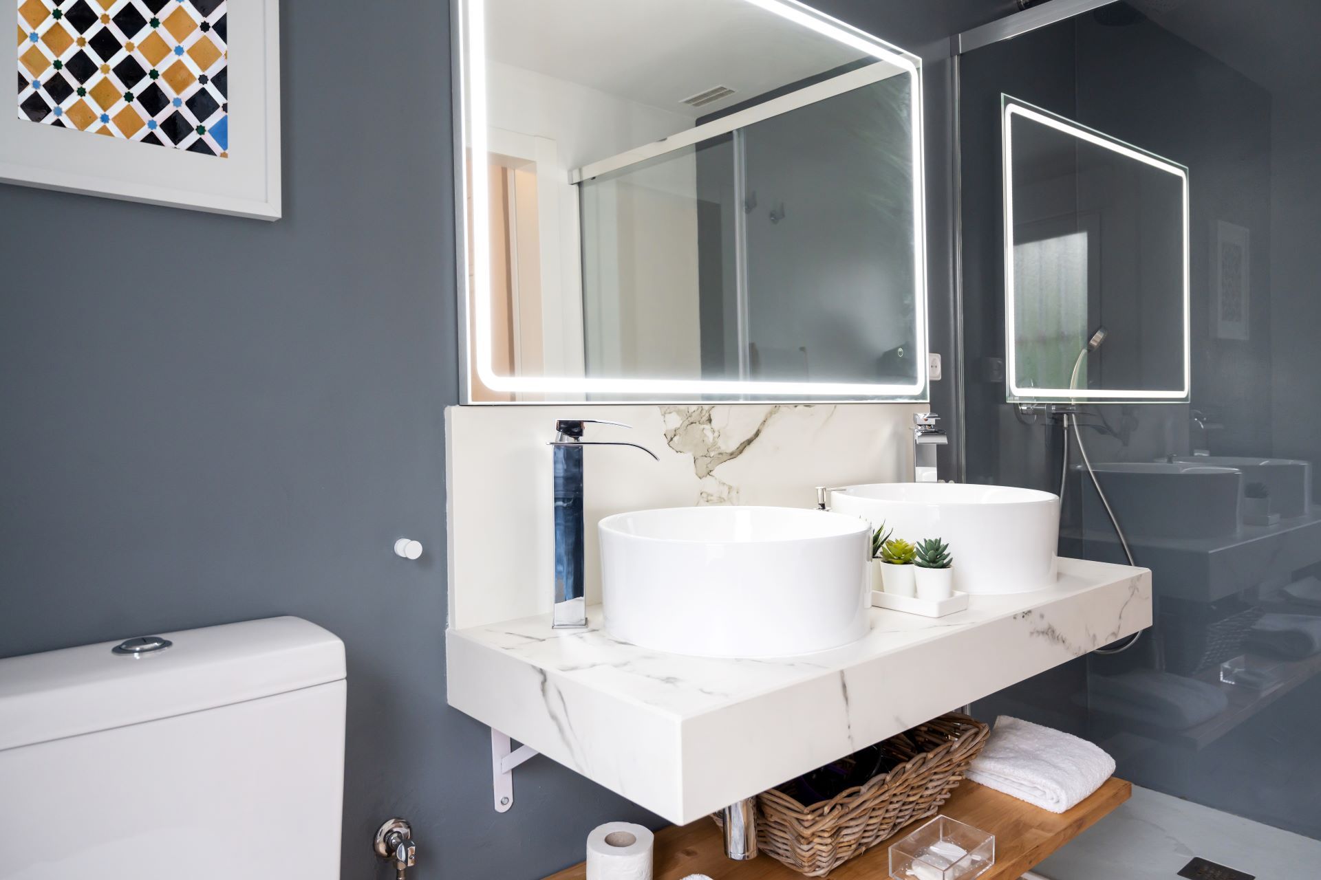 A bathroom vanity with white rectangular sinks, a large mirror, black pendant lights, and teal and gold scalloped tile walls.