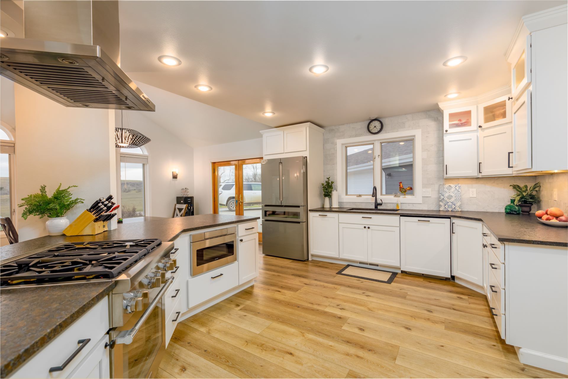 Bright white kitchen with stainless steel appliances, wood floors, and a center island under recessed lights