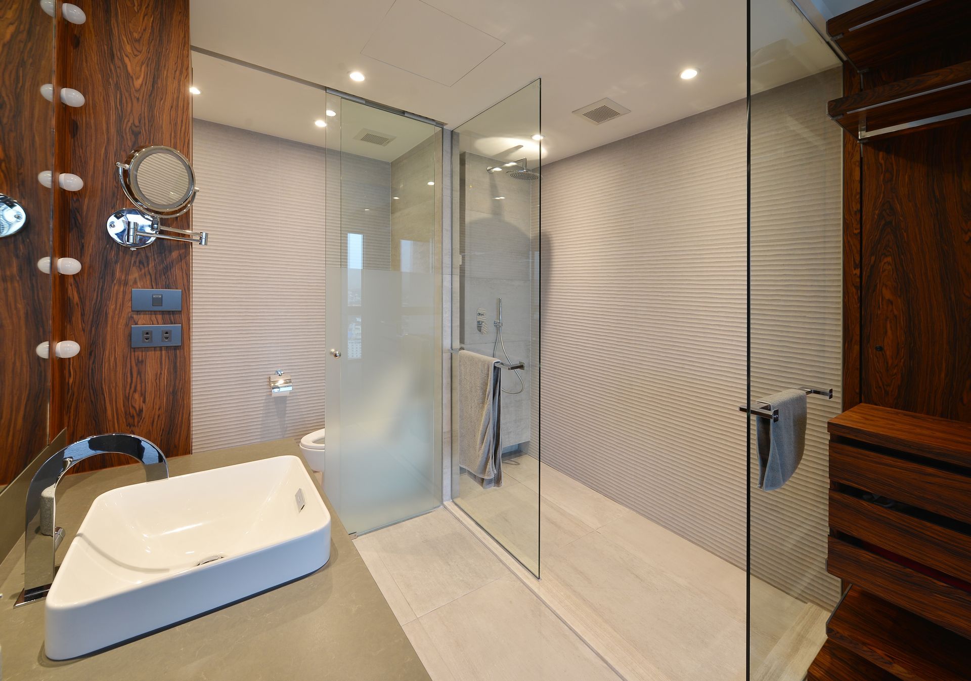 Modern bathroom with glass shower, wooden accents, and patterned wall.