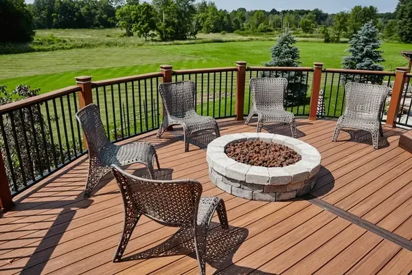 A wooden deck with wicker chairs surrounding a fire pit, overlooking a grassy field.