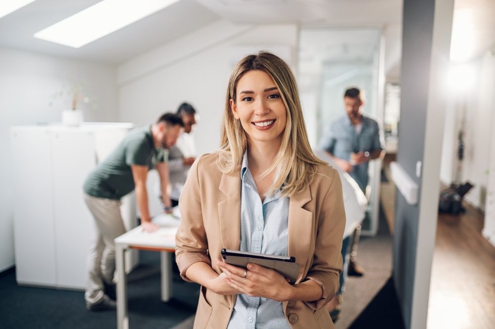 A woman is holding a tablet and smiling in an office.