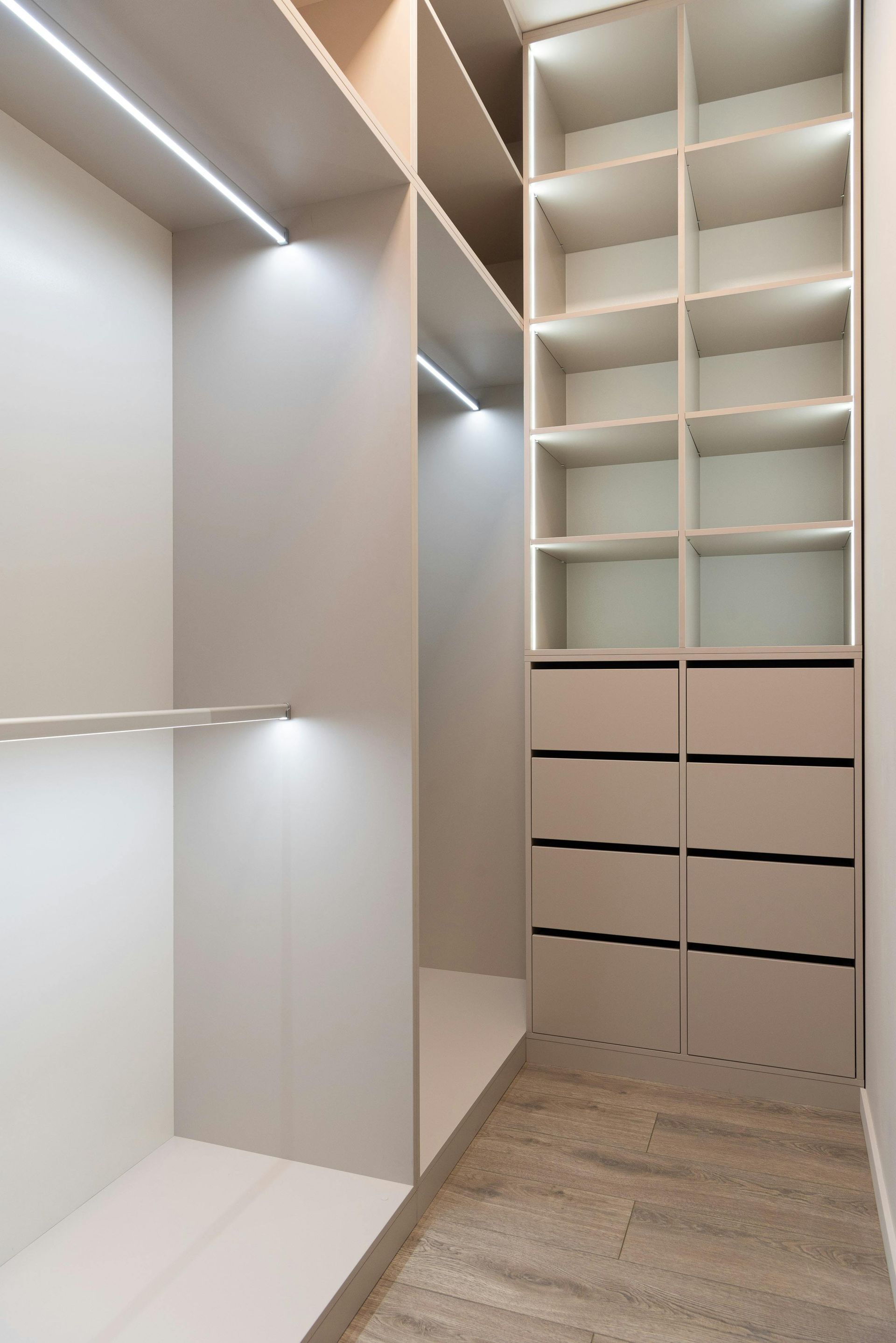 Walk-in closet with shelves and drawers. Soft lighting illuminates the neutral-toned interior and flooring.