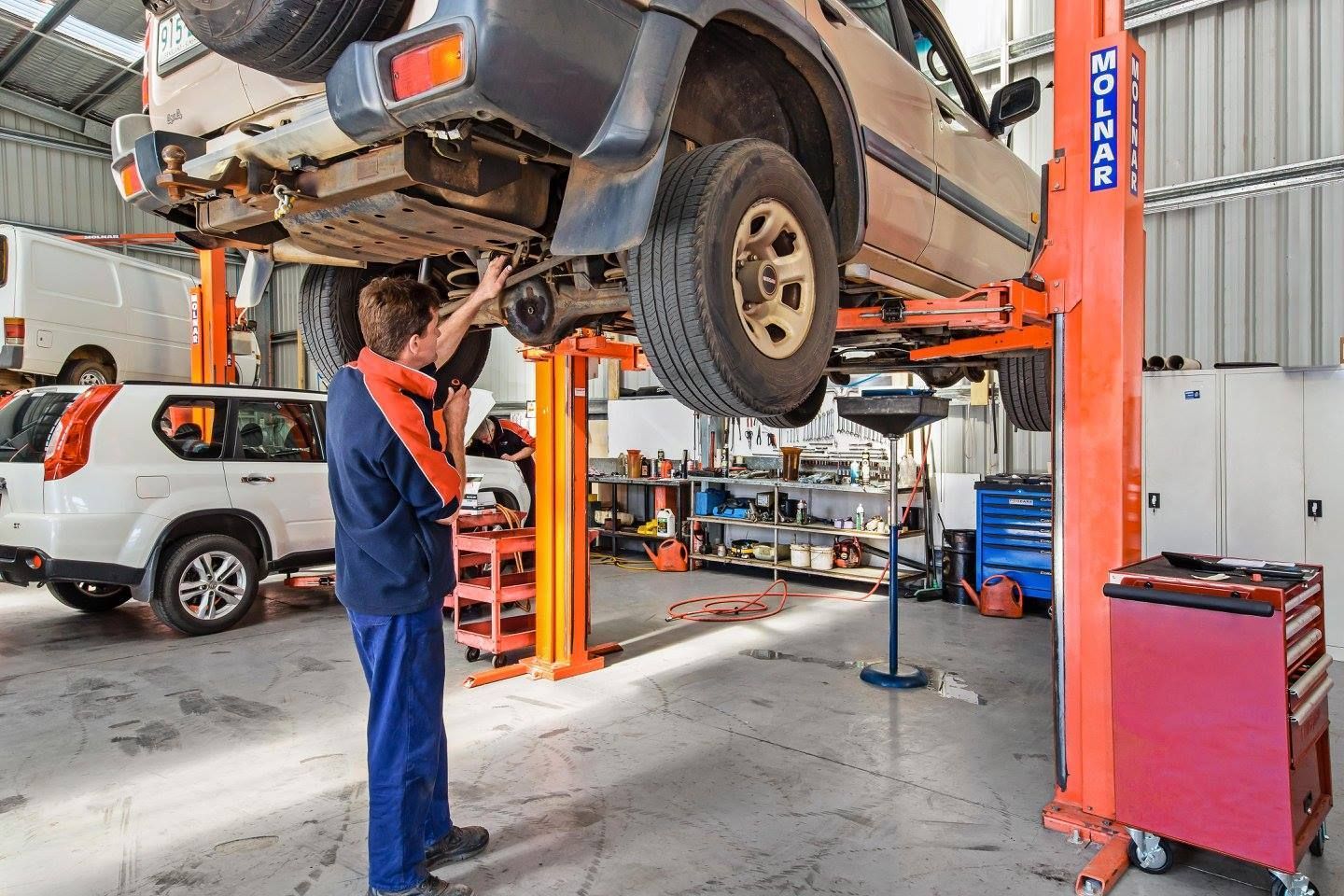 A man is working on a car on a lift in a garage.