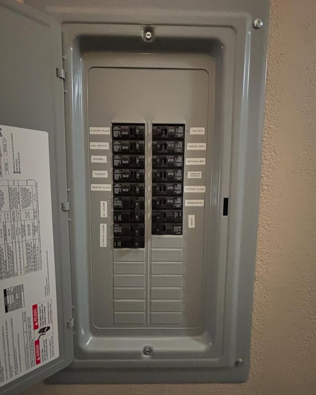 Open gray electrical panel with circuit breakers and labels.