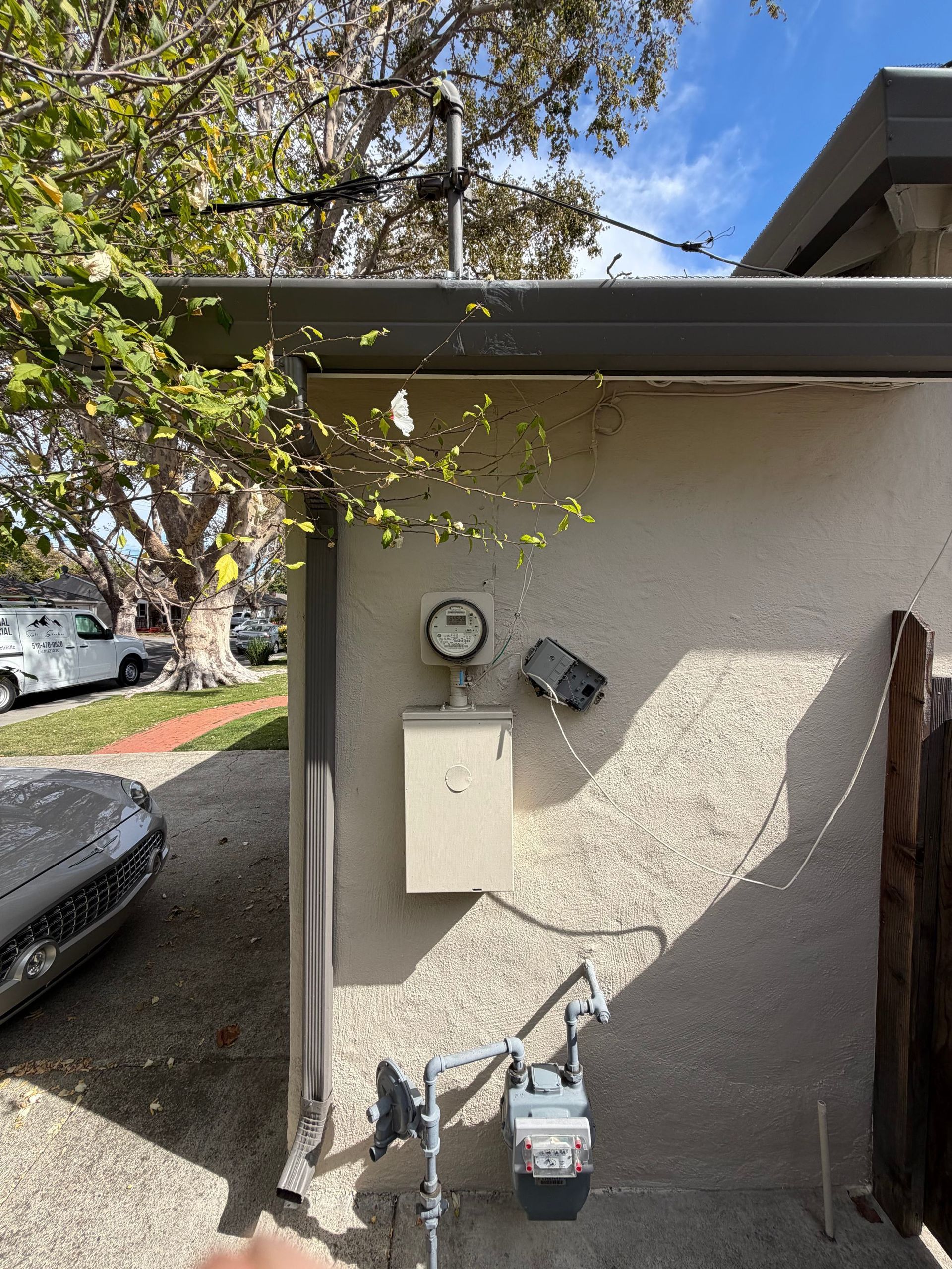 Outdoor house wall with electric meter, white utility box, and gas meter beside a driveway