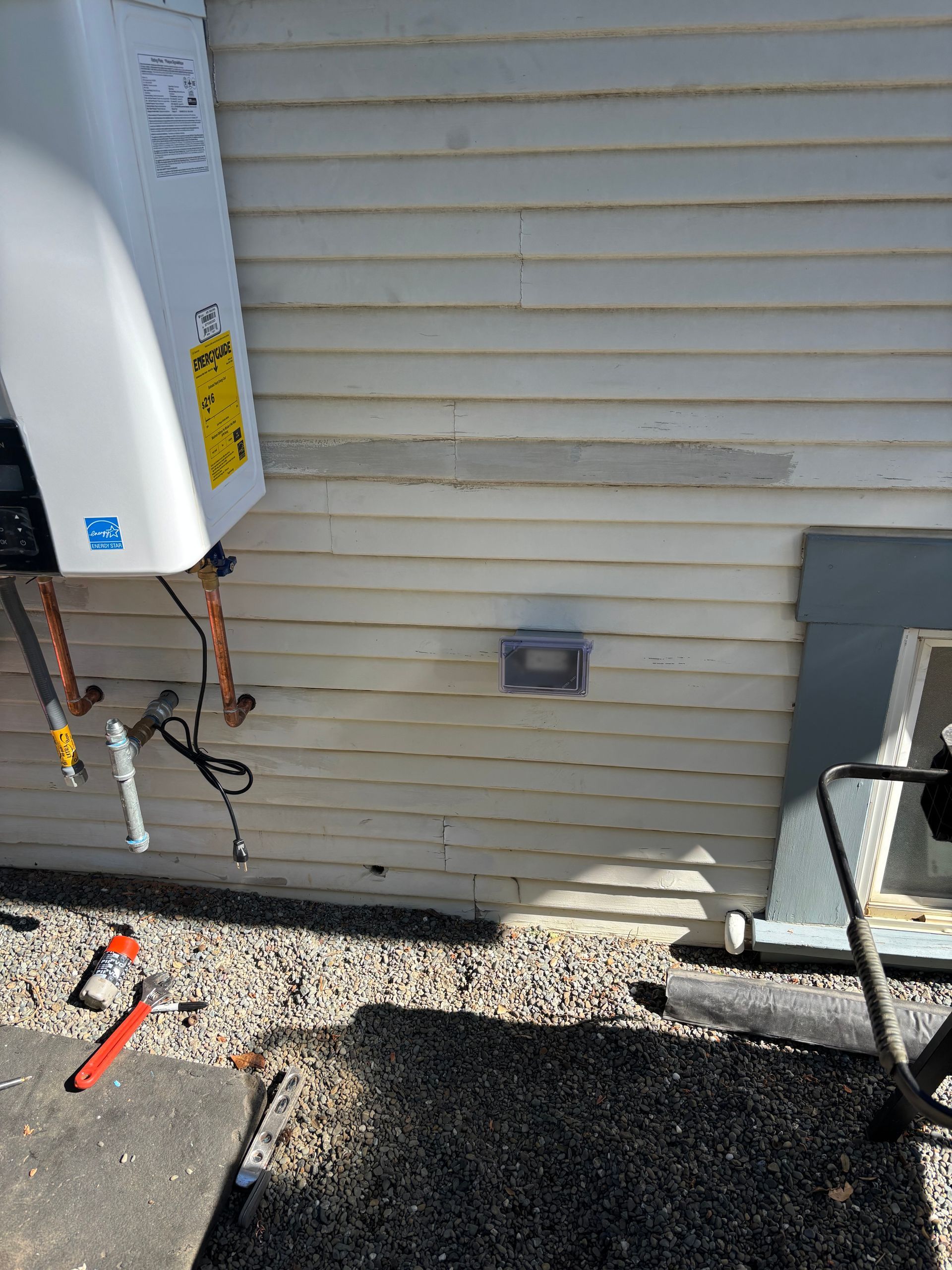 White siding on a building with an outdoor vent.  A heating unit is mounted to the wall with tools scattered below.