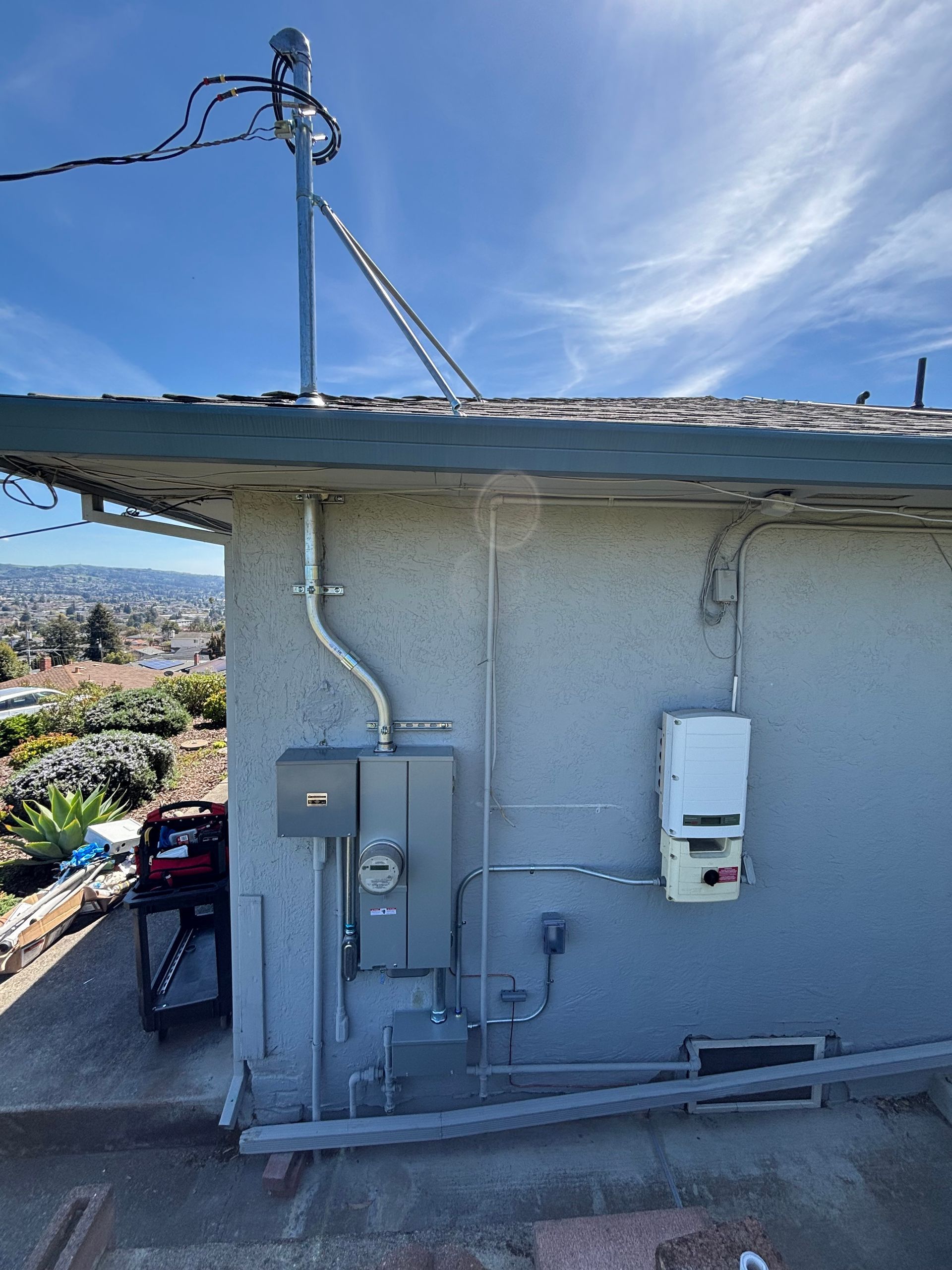Solar panel electrical equipment installed on a stucco building exterior. Conduit, meter, and inverter. Clear sky background.