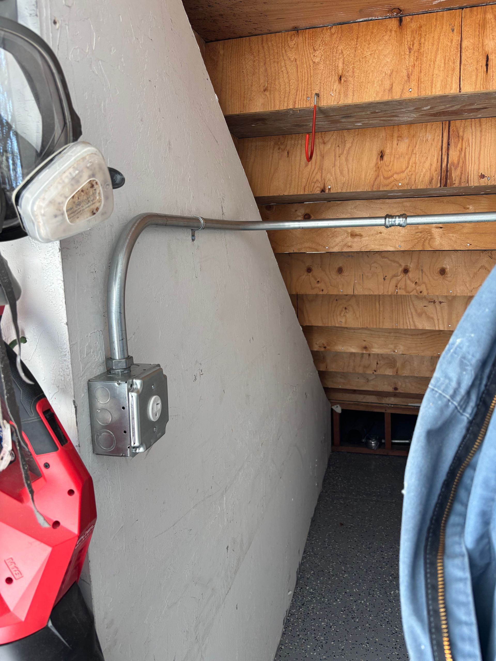 Metal electrical conduit running along a gray wall, leading to a metal outlet box, in a garage.